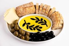 a white plate topped with olives, bread and crackers next to a bowl of dip