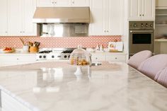 a kitchen with white cabinets and marble counter tops