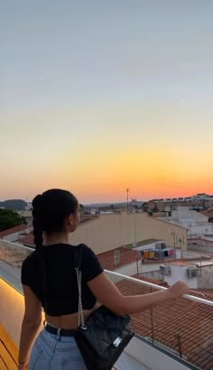 a woman standing on top of a balcony next to a building with a sunset in the background