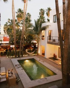 an outdoor swimming pool surrounded by palm trees and lights at dusk with chairs around it