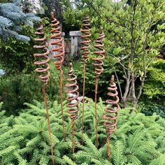 some very pretty metal flowers in the middle of some bushes and trees with lots of green leaves