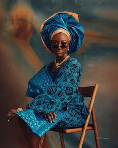 a woman sitting on top of a wooden chair wearing a blue dress and head scarf