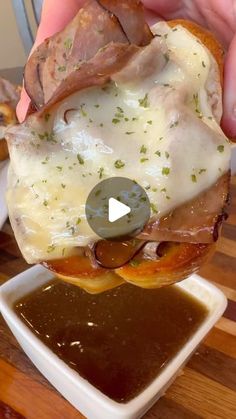 someone is holding up a sandwich with meat and cheese on it in front of some dipping sauce