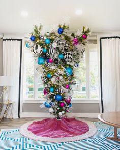 a christmas tree with ornaments in the middle of it on a rug next to a window