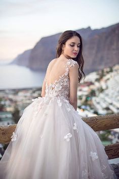 a woman in a wedding dress standing on a balcony looking at the ocean and mountains