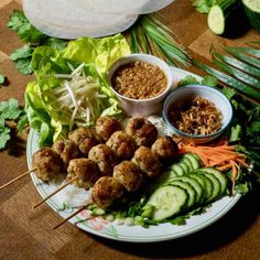 a plate with meatballs, cucumbers and carrots on it next to other foods