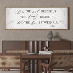 a dining room table with chairs and a framed sign above it that says, but the food before us, the family beside us, and the life between us