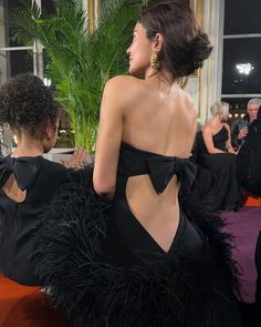 the back of a woman in a black dress with large feathers on it's skirt