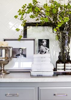 a bathroom counter topped with lots of pictures and flowers next to a vase filled with green leaves