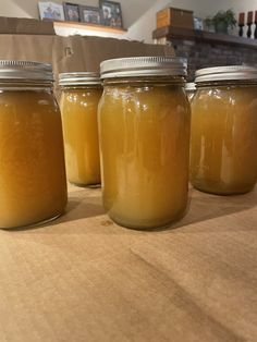 four jars filled with yellow liquid sitting on top of a wooden table next to boxes