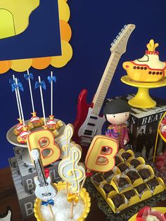 a table topped with cakes and cupcakes next to a guitar shaped cake on top of a wooden table