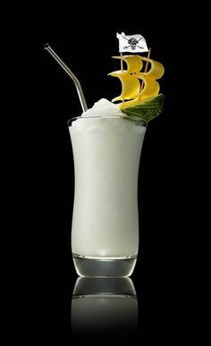 a tall glass filled with white liquid and topped with a pirate ship garnish