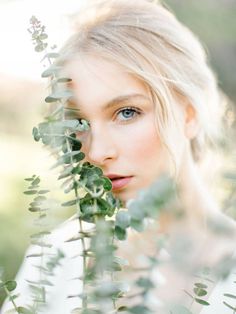 a woman with blonde hair and blue eyes is looking at the camera while surrounded by greenery