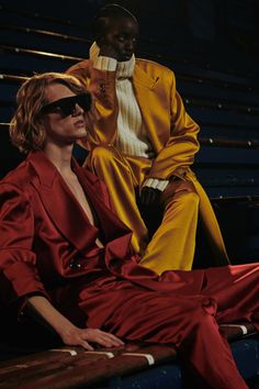 two people sitting on the bleachers in red and yellow outfits, one wearing sunglasses