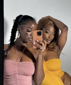 two beautiful women standing next to each other in front of a mirror looking at their cell phones