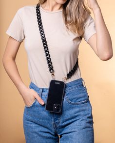 a woman wearing a white shirt and blue jeans holding a cell phone in her right hand