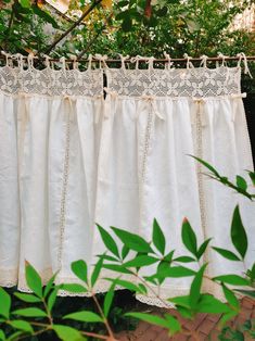 a white curtain hanging from a tree outside with green leaves in the foreground and an open window behind it