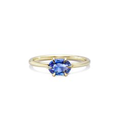 a yellow gold ring with an oval blue sapphire stone in the center, on a white background