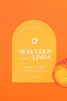 an orange and yellow save the date card next to a red flower on an orange background