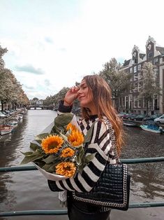 a woman standing on a bridge with flowers in her hand and looking into the distance