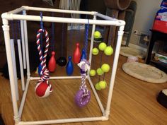 a toy cage with balls and toys hanging from it's sides on a wooden floor