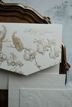 an ornate white and gold wedding card with birds on it, sitting on a bed