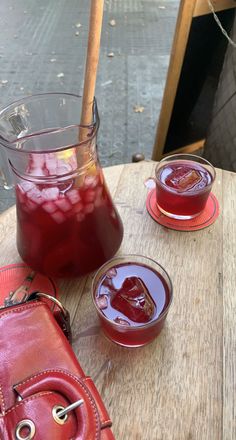 two glasses filled with liquid sitting on top of a wooden table next to a red purse