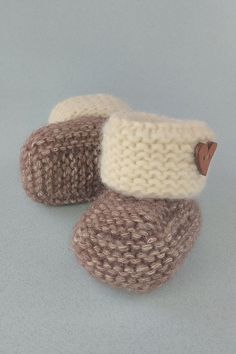 two knitted slippers are shown on a gray surface, one is brown and the other is white