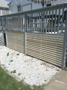 an umbrella sitting on top of a wooden fence next to a yard with gravel and grass