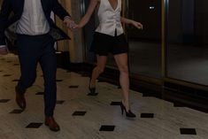 a man and woman are walking down the hall holding hands while dressed in business attire