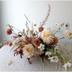 a vase filled with lots of flowers on top of a white cloth covered tablecloth