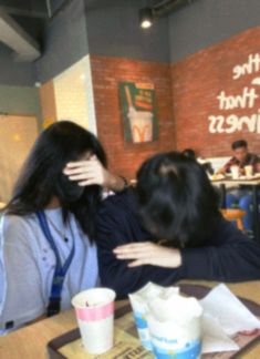 two people sitting at a table with their arms around each other and one woman covering her face