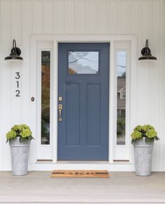 two planters with flowers are on the front step of a house that is painted white and blue