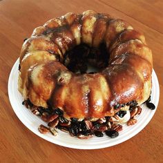 a bundt cake with pecans and raisins on a white plate sitting on a wooden table