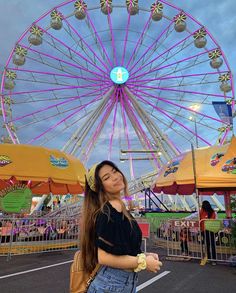 a woman standing in front of a ferris wheel at an amusement park with her hand on her hip