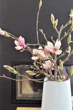 a white vase filled with pink flowers on top of a wooden table