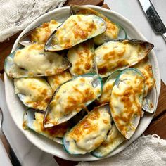 a white plate topped with mussels covered in cheese on top of a wooden table