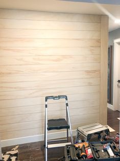 a ladder and some tools on the floor in front of a wall with wood planks