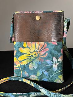 a purse with a flower print on it and a brown leather strap is sitting on a black surface