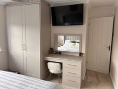 a bedroom with a bed, dresser and television mounted on the wall above it's headboard