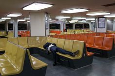 a man laying on top of a yellow bench in a room filled with orange and black seats