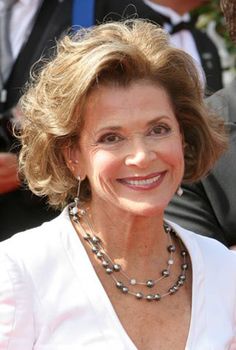 an older woman smiling at the camera with other people in the back ground behind her