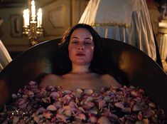 a woman sitting in a bathtub filled with seashells next to a chandelier