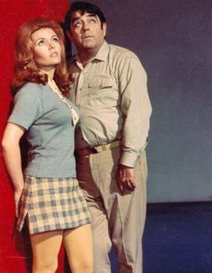 a man and woman standing next to each other in front of a red wall,