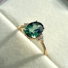 a green ring sitting on top of a white velvet covered surface with diamonds around it