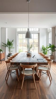 a large wooden table surrounded by chairs and potted plants in front of a window