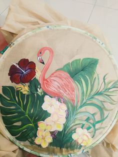 a painted plate with a flamingo and tropical flowers on the front is being held by someone's hand