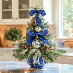 a blue and white christmas tree in a vase on a kitchen counter with pine cones