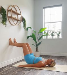 a woman is doing yoga on a mat in front of a wall with potted plants