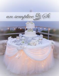 a wedding cake sitting on top of a table covered in white cloths and flowers